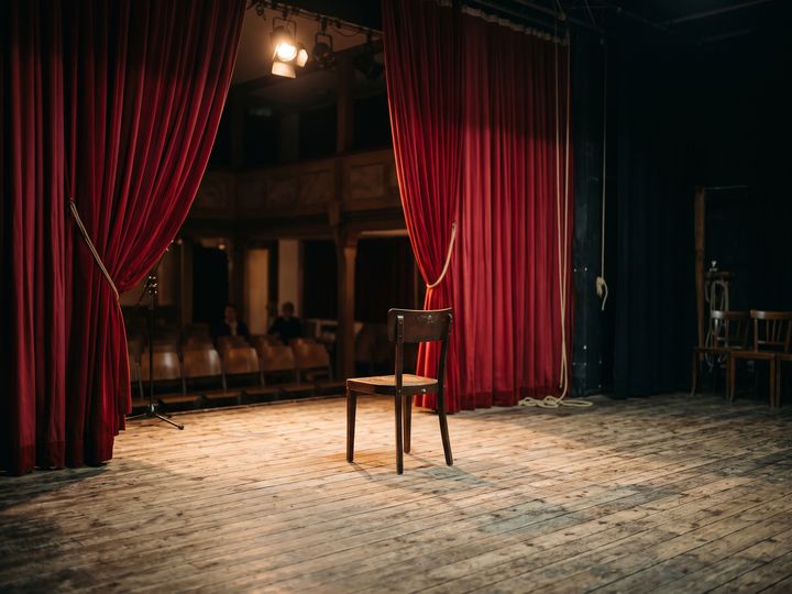 Image d’illustration : Scène de théâtre vide avec rideau rouge et une chaise sous le projecteur