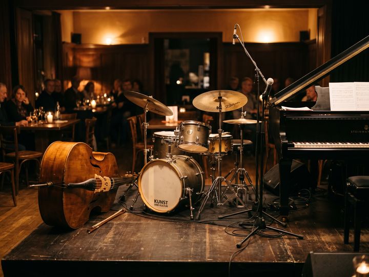 Image d’illustration : Contrebasse, batterie et piano à queue sur une petite scène de jazz